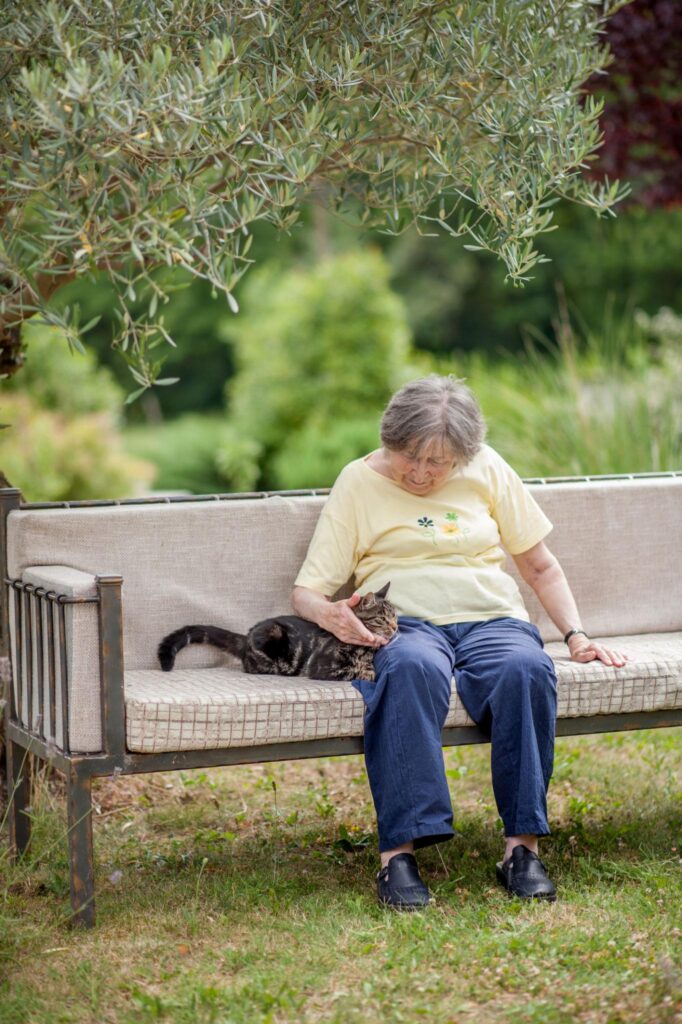 senior lady petting striped cat on couch outdoors